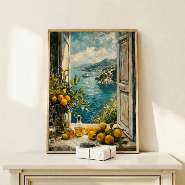 May include: Framed artwork displaying an open window view of the Amalfi Coast with turquoise waters, mountainous coastline, and a windowsill arrangement of fresh lemons, olive oil bottles, and Mediterranean plants. The painting features realistic brushwork in blues, yellows, and earth tones. A small white wrapped package sits beneath the wooden-framed print on a light wooden shelf against a cream wall.