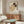 May include: Framed Egon Schiele artwork showing two embracing figures with reddish and dark hair on cream background, displayed above walnut credenza in modern living room with white sculptural chair, oval glass coffee table, and warm natural lighting