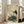 May include: Framed vintage-style Japanese artwork featuring a white stork with dark wing tips standing beside a brown turtle on blue rocks with green plants. The print has aged beige background with traditional Asian calligraphy and red seals. Light wood frame leans against white wall next to beige sectional sofa in bright modern living room with large windows.