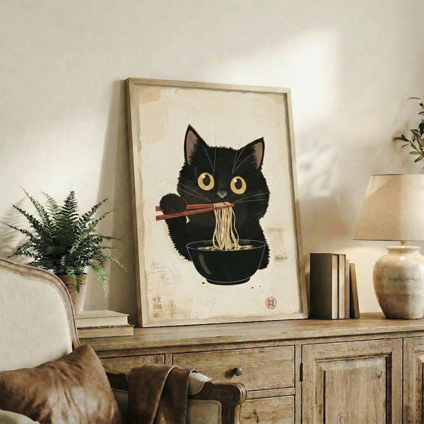 May include: Framed artwork displayed on rustic wooden credenza showing black cat with golden eyes eating ramen noodles with chopsticks from dark bowl, rendered in Japanese ukiyo-e woodblock print style on cream textured paper. Scene includes fern plant, ceramic vases, books, and beige armchair in warm-toned living room setting.