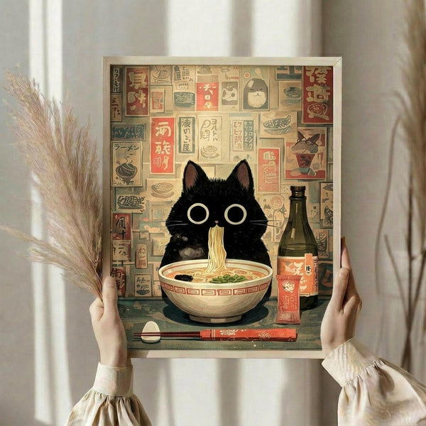 May include: Person holding framed artwork showing adorable black cat with large round eyes sitting behind bowl of ramen noodles, surrounded by colorful Japanese text blocks and food illustrations. Vintage-style poster in neutral frame against white curtained window, with dried pampas grass visible to left. Warm, cozy home decor styling.