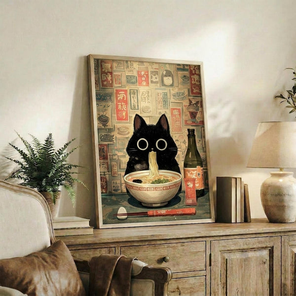 May include: Framed poster artwork featuring a black cat with large white eyes sitting behind a bowl of ramen noodles, with chopsticks and a bottle nearby. Background shows vintage Japanese restaurant advertisements and signage in warm tones. Print displayed on rustic wooden console table alongside books, ceramic vase, and fern plant in cozy living room setting with beige upholstered furniture.