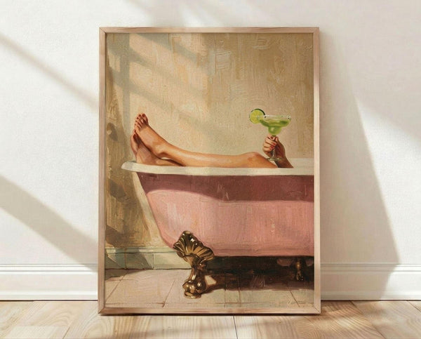 May include: Framed vintage-style poster showing a person's legs relaxing in a pink clawfoot bathtub, holding a green margarita cocktail with lime garnish. The artwork has warm, muted tones with soft lighting streaming through a bathroom window. The wooden frame sits on light wooden flooring against a white wall with natural shadows cast across the scene.
