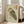 May include: Framed Japanese woodblock-style owl print in light wooden frame, leaning against white wall next to beige upholstered chair. The artwork features a detailed owl with mottled brown and green plumage on pale green background, with red Japanese calligraphy characters in upper right corner. Natural daylight streams through nearby windows onto hardwood floors in minimalist living room setting.