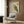 May include: A framed Japanese woodblock print of an owl with detailed brown and green feathers and Japanese calligraphy, displayed on a wood-paneled wall above a beige upholstered armchair with geometric patterned pillow. Scene includes a modern brass floor lamp and dark round side table with open book near a window with curtains.