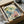 May include: Framed botanical watercolor print featuring delicate flowers in soft blues, greens, and coral pink tones, displayed in black frame inside cardboard shipping box with protective tissue paper wrapping on white surface
