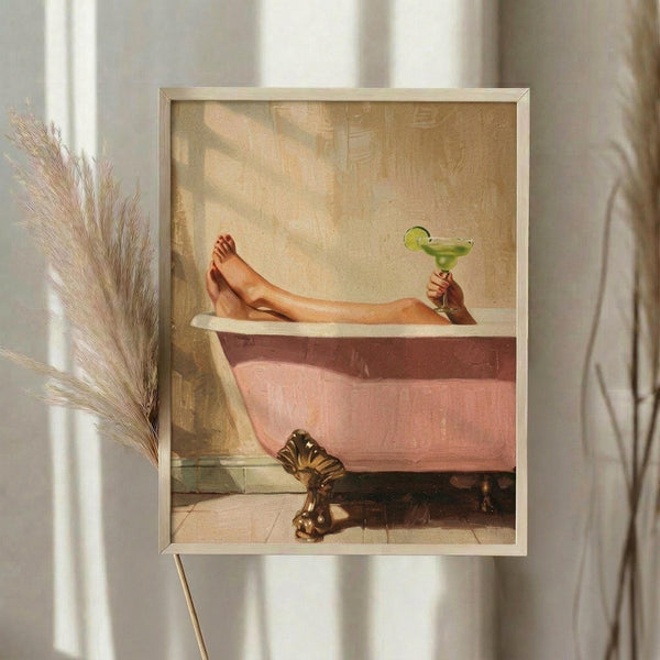May include: Framed artwork showing person's legs relaxing in pink clawfoot bathtub, holding green margarita cocktail, displayed on light wall next to dried pampas grass stems. Warm vintage-style illustration in golden wood frame with soft natural lighting from nearby window.