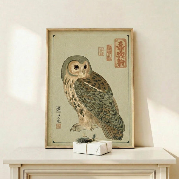 May include: Framed Japanese woodblock-style owl print in natural wood frame, displayed on light wooden shelf. The artwork features a detailed brown and green owl with large round eyes against pale background, with red Japanese calligraphy characters in upper right corner. Small wrapped white gift box with evergreen sprig sits beside the frame on the shelf.