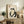 May include: Japanese-style artwork in light wood frame showing black ink frog holding small bowl, with red seal stamp above, displayed on rustic wooden sideboard beside fern plant, ceramic vase, and stacked books in neutral-toned living room setting
