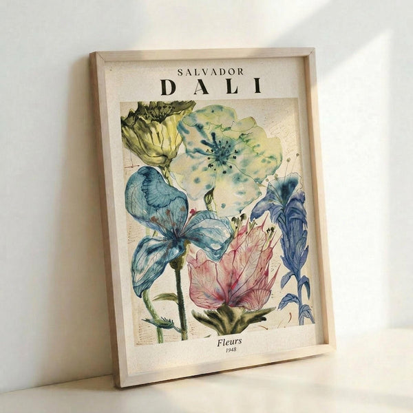 May include: A framed art print leaning against a white wall, featuring Salvador Dali's colorful floral illustration with blue, pink, yellow and green watercolor flowers on a cream background. The wooden frame sits on what appears to be a white surface, with soft natural lighting creating gentle shadows.