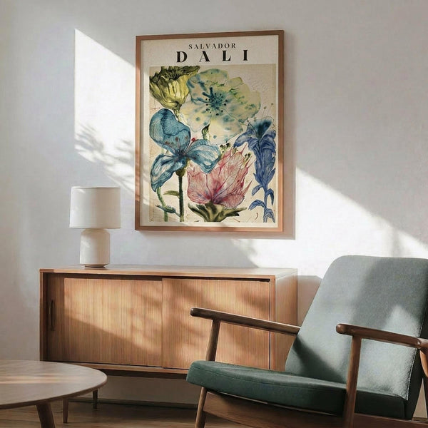 May include: Salvador Dali botanical poster with colorful flowers in yellow, blue, pink and green watercolor style, displayed in wooden frame above mid-century modern credenza. Gray upholstered armchair with wooden arms sits nearby, white table lamp on sideboard. Warm sunlight creates shadows on white wall in contemporary living room setting.