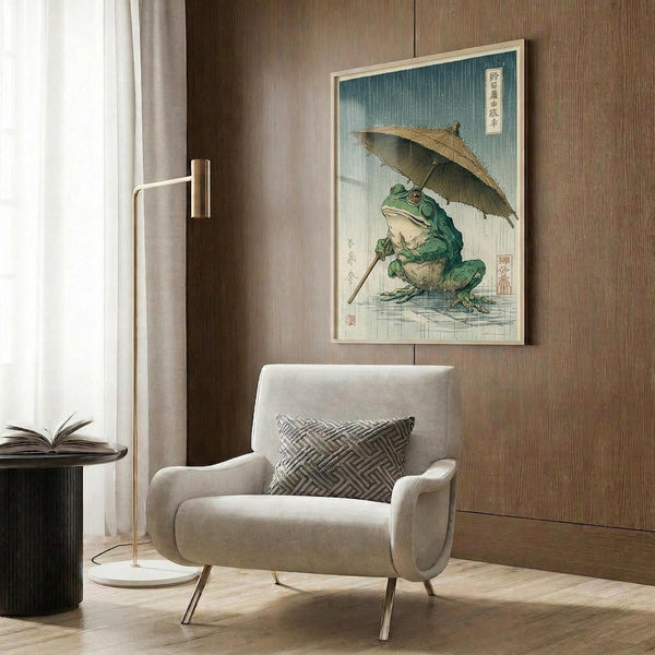 May include: Japanese woodblock print artwork featuring a green frog holding a bamboo umbrella in falling rain, displayed in light wooden frame on textured brown wall panel above cream upholstered armchair with geometric patterned pillow, alongside modern brass floor lamp and dark round side table with open book