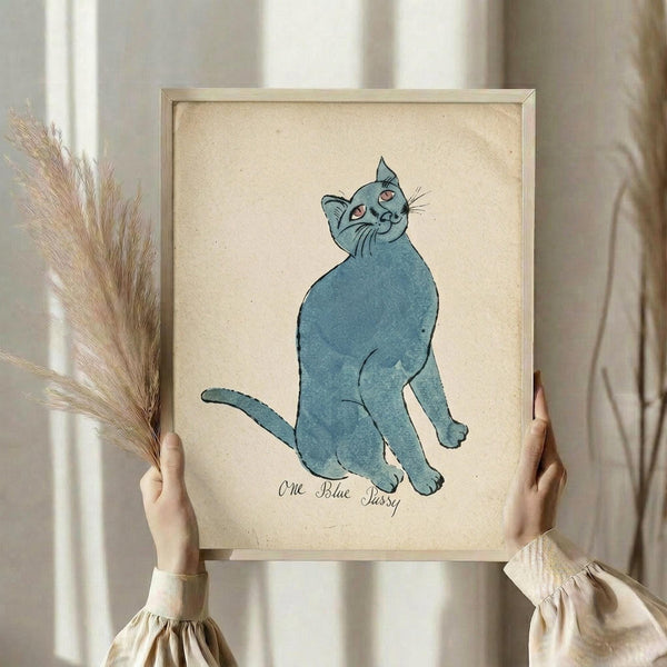 May include: Person in cream ruffled sleeves holding framed artwork and dried pampas grass against white curtained window. The vintage-style poster features a blue watercolor cat sitting upright with pink eyes on aged beige paper, displayed in light wood frame. Soft natural lighting creates warm, aesthetic home decor styling.
