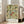 May include: Framed botanical art print with intricate floral pattern featuring green leaves, golden scrollwork, red berries, and cream flowers in William Morris Victorian style, displayed against white wall next to beige upholstered chair in bright living room with large windows and natural light streaming across wooden floors.
