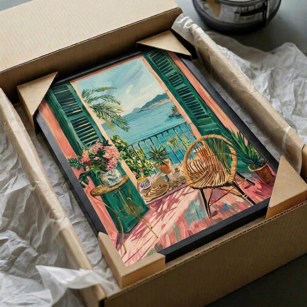 Vintage-style poster artwork depicting a Mediterranean balcony scene with green shuttered windows opening to an ocean view. Features a wicker peacock chair, potted palm plants, pink bougainvillea flowers, and terracotta planters on coral-pink tiled flooring. The illustration uses soft pastels and has a nostalgic 1950s aesthetic. Shown unframed in a black frame within shipping packaging with protective wrapping.