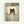 May include: Framed artwork showing a black kitten with large golden eyes reading a small orange book while tucked into bed with white pillows and green striped bedding. The illustration has a soft, painted style with muted earth tones and is displayed in a light wood frame against a white wall.