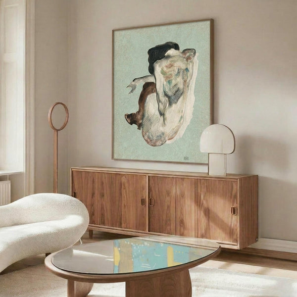 May include: Framed art print of a curled nude figure in earth tones against pale green background, displayed above mid-century walnut credenza in modern living room with cream chair, brass floor lamp, oval glass coffee table, and white walls with natural sunlight