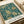 May include: Victorian-style botanical poster with intricate teal and cream floral pattern featuring chrysanthemums, sunflowers, and decorative leaves in an ornate Arts and Crafts design. The print appears matted in cream with "Morris & Company 1866" and "William Morris" text at bottom, displayed on white paper with neutral ribbon beside it on a wooden surface.