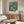 May include: William Morris chrysanthemum pattern poster in teal and gold botanical design displayed above walnut mid-century modern credenza in minimalist living room. White sculptural chair and oval glass coffee table visible. Warm natural lighting creates shadows on cream walls.