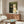 May include: Framed artwork showing two cats in formal wedding attire - a black cat with gold collar and white cat with pink bow tie holding yellow flowers, displayed above a walnut wood credenza in a modern living room with white curved chair, glass coffee table, and neutral walls