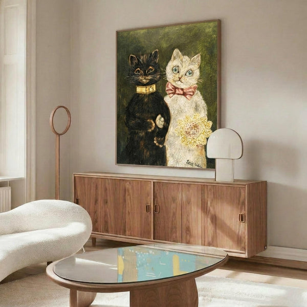 May include: Framed artwork showing two cats in formal wedding attire - a black cat with gold collar and white cat with pink bow tie holding yellow flowers, displayed above a walnut wood credenza in a modern living room with white curved chair, glass coffee table, and neutral walls