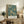 May include: Framed poster with teal background and ornate golden floral pattern featuring chrysanthemums, leaves, and botanical motifs in William Morris Victorian style, displayed on rustic wooden sideboard next to fern plant, books, ceramic vase, and leather chair in cozy living room setting with cream walls