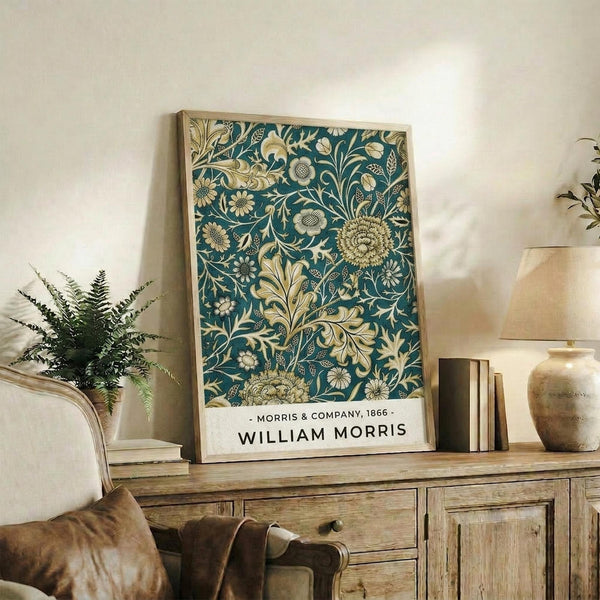 May include: Framed poster with teal background and ornate golden floral pattern featuring chrysanthemums, leaves, and botanical motifs in William Morris Victorian style, displayed on rustic wooden sideboard next to fern plant, books, ceramic vase, and leather chair in cozy living room setting with cream walls