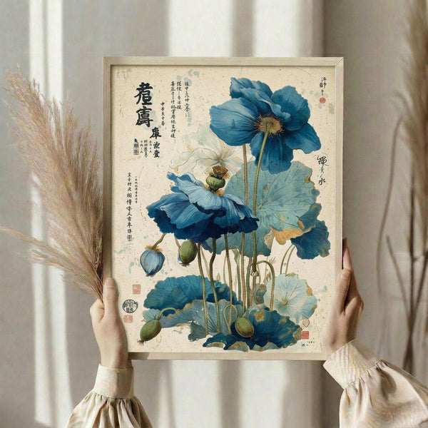 May include: hands holding a framed botanical print featuring vibrant blue poppies with stems, leaves, and seed pods against aged beige paper. Asian calligraphy text appears on the left side with red seal stamps. Person wears cream-colored ruffled sleeves while displaying the artwork near dried pampas grass and white curtains in soft natural lighting.
