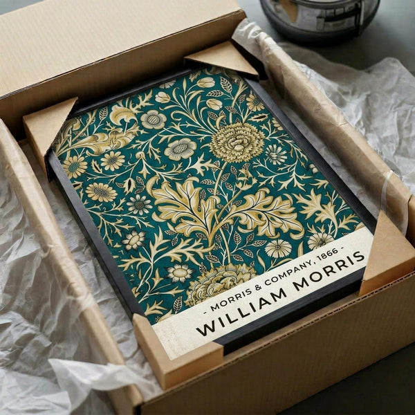 May include: Framed William Morris floral pattern print in teal and gold, featuring ornate chrysanthemums and decorative foliage, displayed in black frame inside open cardboard shipping box with tissue paper wrapping, surrounded by natural lighting on neutral surface.