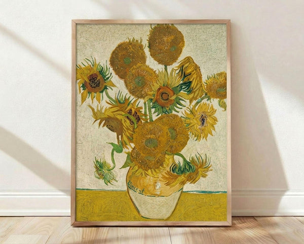 May include: Framed reproduction of Van Gogh's famous sunflowers painting displayed on wooden floor against white wall. The artwork shows vibrant yellow sunflowers in various stages of bloom arranged in a simple vase, painted in Van Gogh's distinctive thick brushstroke style with golden yellow background. Natural wood frame complements the warm tones of the impressionist masterpiece.
