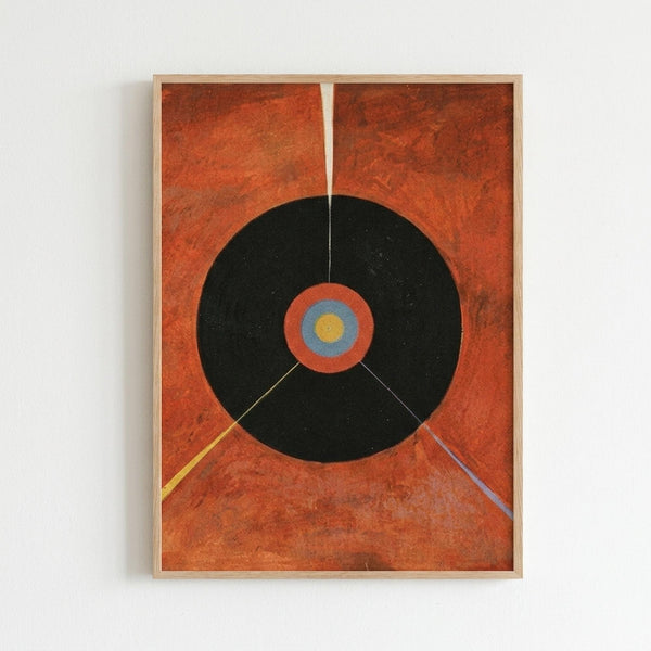 Framed abstract artwork featuring a large black circle on a textured orange-red background. The circle contains concentric rings in orange, blue, and yellow at its center. Two diagonal lines extend from the circle - one yellow and one purple. The piece is displayed in a light wood frame against a white wall, showing visible texture and brushwork throughout the composition.