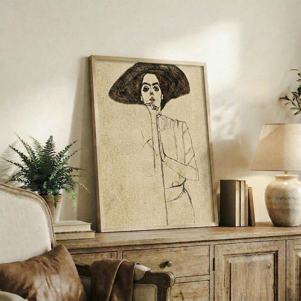 May include: Framed print of a woman with dark hair and hat in sketch style, displayed on rustic wooden console table alongside fern plant, books, ceramic vase, and brown leather chair in warm-toned living room setting