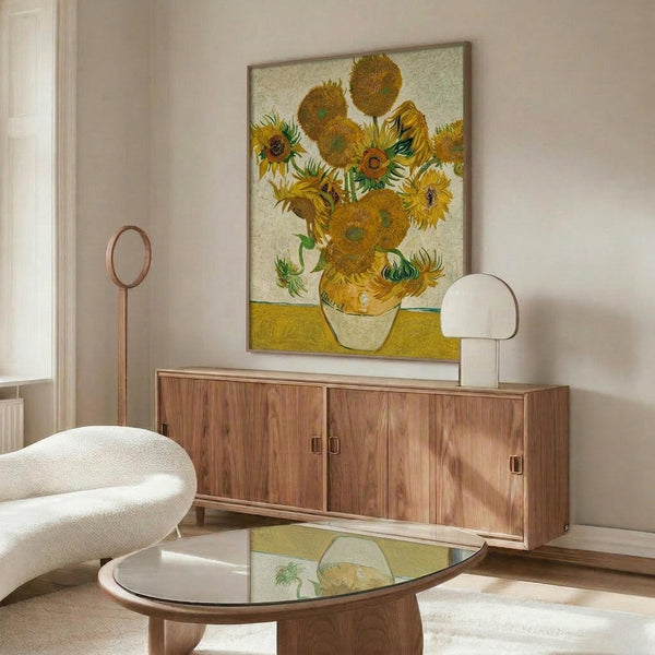 May include: Van Gogh's famous sunflowers painting displayed above a mid-century modern walnut credenza in a bright living room. The artwork shows yellow sunflowers in a vase against a cream background with yellow table surface. White upholstered chair and glass coffee table complete the stylish interior setting with natural sunlight streaming across wooden floors.