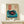 May include: Framed vintage-style poster featuring a turquoise record player with black vinyl and red center label, displayed on light wood shelf. Poster has cream background with red Japanese characters and text block in upper portion. Small white wrapped gift with evergreen sprig sits beside the wooden frame. Clean, minimalist styling against white wall.