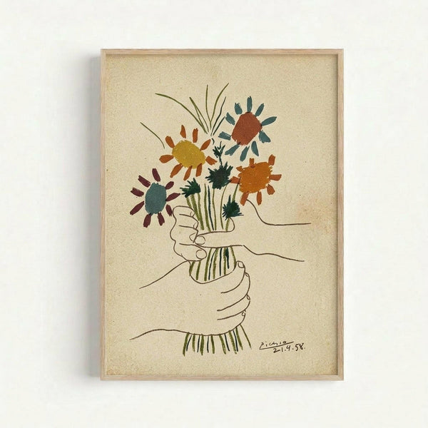 Framed artwork showing a line drawing of two hands holding a bouquet of colorful flowers including daisies and wildflowers in yellow, orange, red, teal, and green watercolor-style paint. The minimalist sketch is signed and dated, displayed on cream-colored paper in a light wood frame against a white wall.