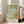 May include: Large framed botanical poster featuring William Morris's ornate floral pattern in sage green, golden yellow, and turquoise. The design shows intricate acanthus leaves, flowing vines, and decorative flowers in the Arts and Crafts style. The print is displayed in a light wooden frame leaning against white walls in a bright living room with beige armchair and large windows.