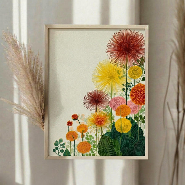 May include: Framed botanical print displaying stylized sunburst flowers in warm autumn colors - red, orange, yellow, and pink blooms with radiating petal patterns alongside green foliage, mounted in light wood frame against cream background. Dried pampas grass visible to left side, soft natural lighting creates gentle shadows on neutral wall.