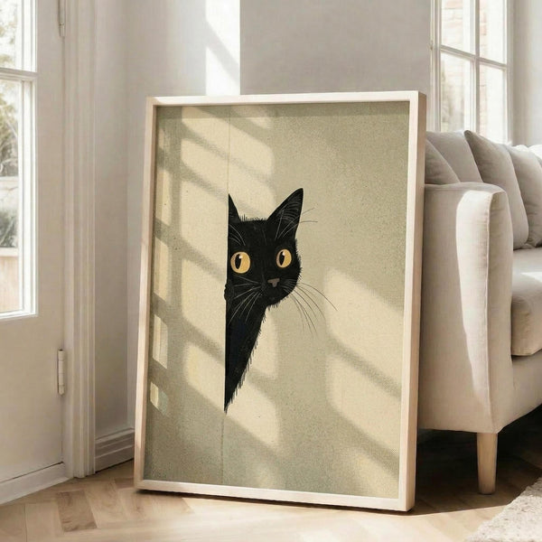 May include: A framed poster print leaning against a white wall next to a beige upholstered chair in a bright living room. The artwork features a black cat with golden yellow eyes peeking from behind what appears to be a white surface or wall. The cat has detailed whiskers and fur texture rendered in a vintage illustration style against a cream-colored background. Natural sunlight streams through tall windows, casting diagonal shadows across the scene.