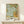 May include: Framed botanical art print featuring ornate acanthus leaves and flowers in sage green, golden yellow, and turquoise colors with Victorian-style decorative flourishes. The print displays "Morris & Company, 1866" and "William Morris" text at bottom. Shown in thin natural wood frame on light wooden shelf against cream wall, with small white wrapped gift box placed in front.