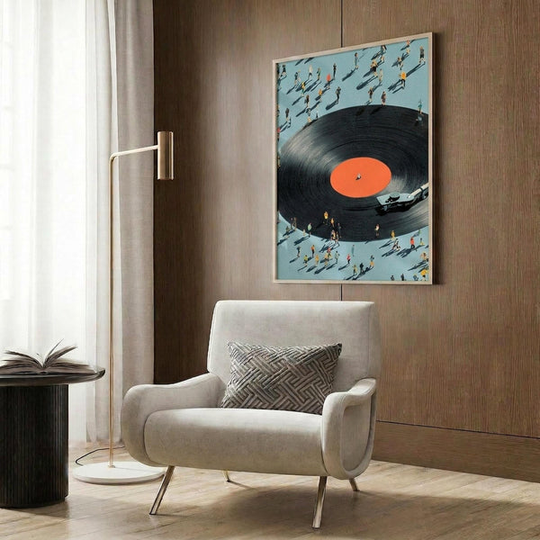 May include: Framed art print showing oversized vinyl record with orange center label surrounded by tiny people figures on light blue background, displayed above beige upholstered chair with geometric patterned pillow in modern living room with wood paneled walls, brass floor lamp, and dark round side table with open book