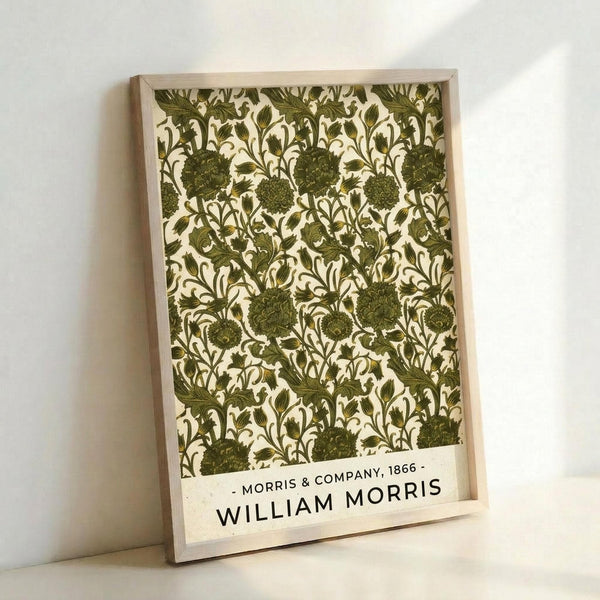 May include: Framed botanical print with intricate green floral pattern featuring detailed flowers, leaves, and vines on cream background. Light wood frame leans against white wall, showing vintage-inspired wallpaper design with dense, repeating motifs in olive and forest green tones.