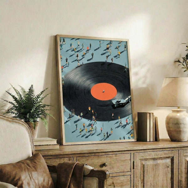 May include: Framed poster displaying a large black vinyl record with orange label surrounded by small people casting shadows on light blue background. Artwork shown in wooden frame on rustic sideboard next to fern plant, books, ceramic vase, and cream chair in modern living room setting.