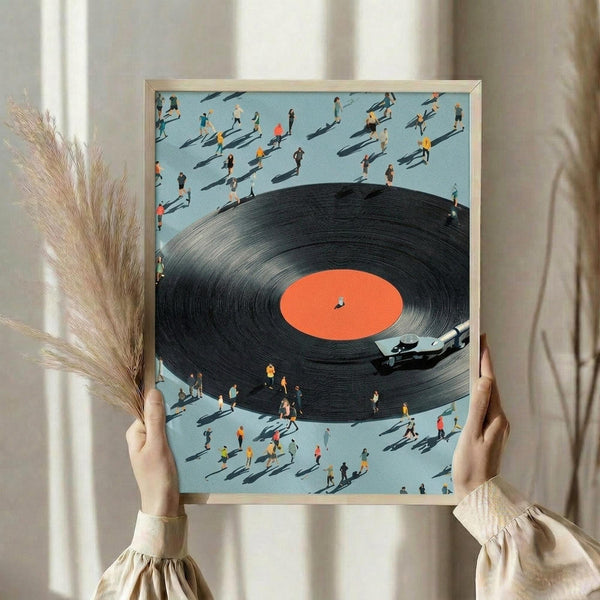 May include: Person holding framed artwork showing large black vinyl record with orange center label surrounded by tiny colorful figures casting long shadows on light blue background. Modern minimalist room setting with dried pampas grass and white curtains. Light wood frame.
