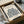 May include: Framed beige art print featuring blue botanical leaf cutout design, displayed in black frame inside cardboard shipping box with white tissue paper and brown packaging materials on neutral surface
