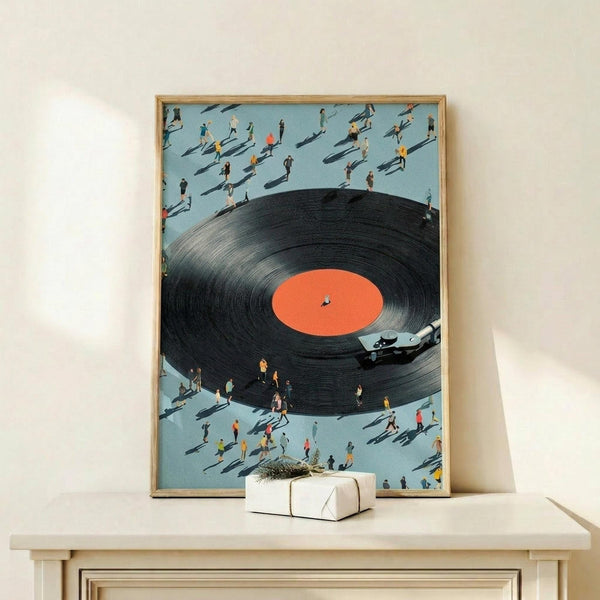 May include: Framed artwork showing a large black vinyl record with orange center label and turntable arm, surrounded by tiny people figures with shadows on light blue background. Natural wood frame displayed on light wood surface next to small wrapped gift box. Contemporary surreal art style with miniature scale contrast.