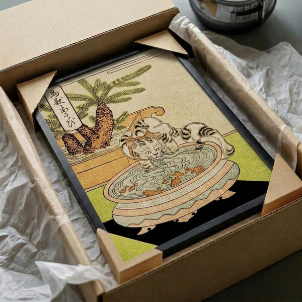 May include: Japanese woodblock print artwork in black frame showing two striped cats sitting in a large wooden bowl with noodles, beside a potted palm plant with Japanese text banner. Print displayed in cardboard shipping box with protective wrapping and wooden frame corners visible. Vintage ukiyo-e style illustration with muted earth tones, greens, and detailed linework typical of traditional Japanese art.