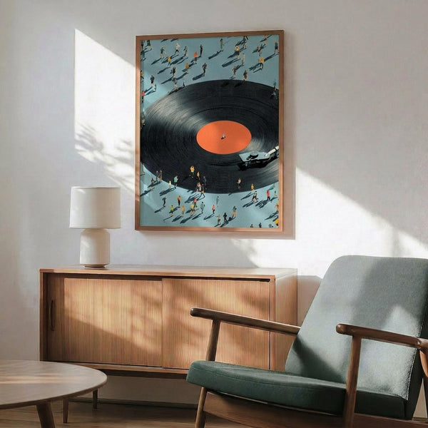 May include: Framed artwork showing a black vinyl record with orange center label surrounded by tiny people casting shadows on a light blue background. The print hangs above a wooden sideboard with white ceramic lamp in a mid-century modern living room with mint green upholstered chair and round coffee table. Natural sunlight creates dramatic shadows across white walls.