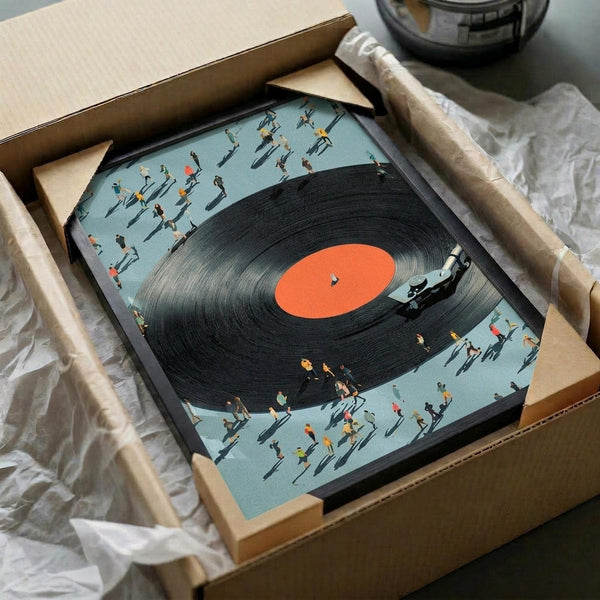 May include: Framed artwork showing a large black vinyl record with orange center label surrounded by tiny people figures casting long shadows on a light blue background. The piece is packaged in a cardboard box with protective wrapping, displayed alongside shipping materials on a white surface with a dark glass object partially visible in the corner.