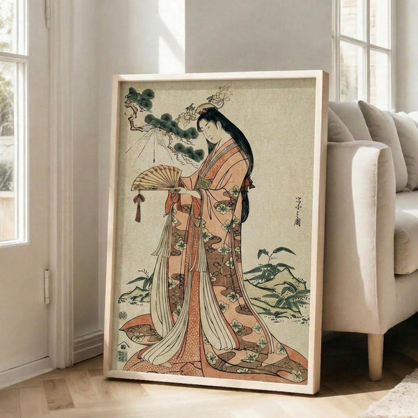 May include: Japanese woodblock print artwork in light wooden frame leaning against white wall next to beige upholstered chair. The vintage illustration depicts a woman in flowing orange and cream kimono with floral patterns, holding a decorative fan, with pine tree branches above. Traditional ukiyo-e art style with muted earth tones on cream background, displayed in bright room with large windows.