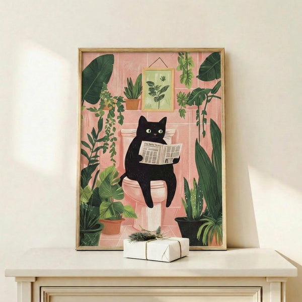 May include: Framed illustration of a black cat with green eyes sitting on a pink toilet while reading a newspaper, surrounded by lush green houseplants including trailing vines and potted plants. The artwork features a coral pink bathroom setting with botanical prints on the wall. Natural wood frame displayed on a light wooden surface beside a small white wrapped gift with greenery accent.
